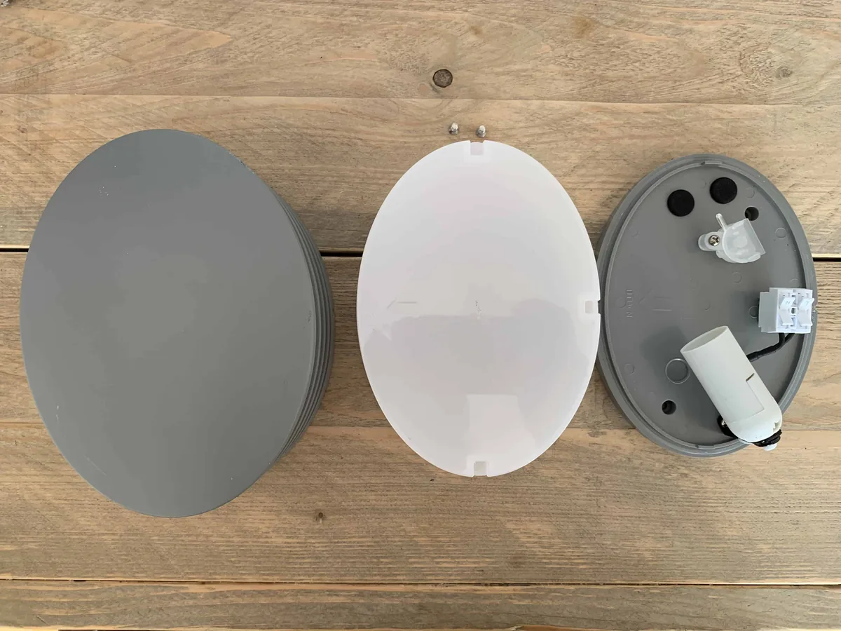 The parts of the fixture: the grey front cover, a white diffuser and the base with the lamp holder and terminal block