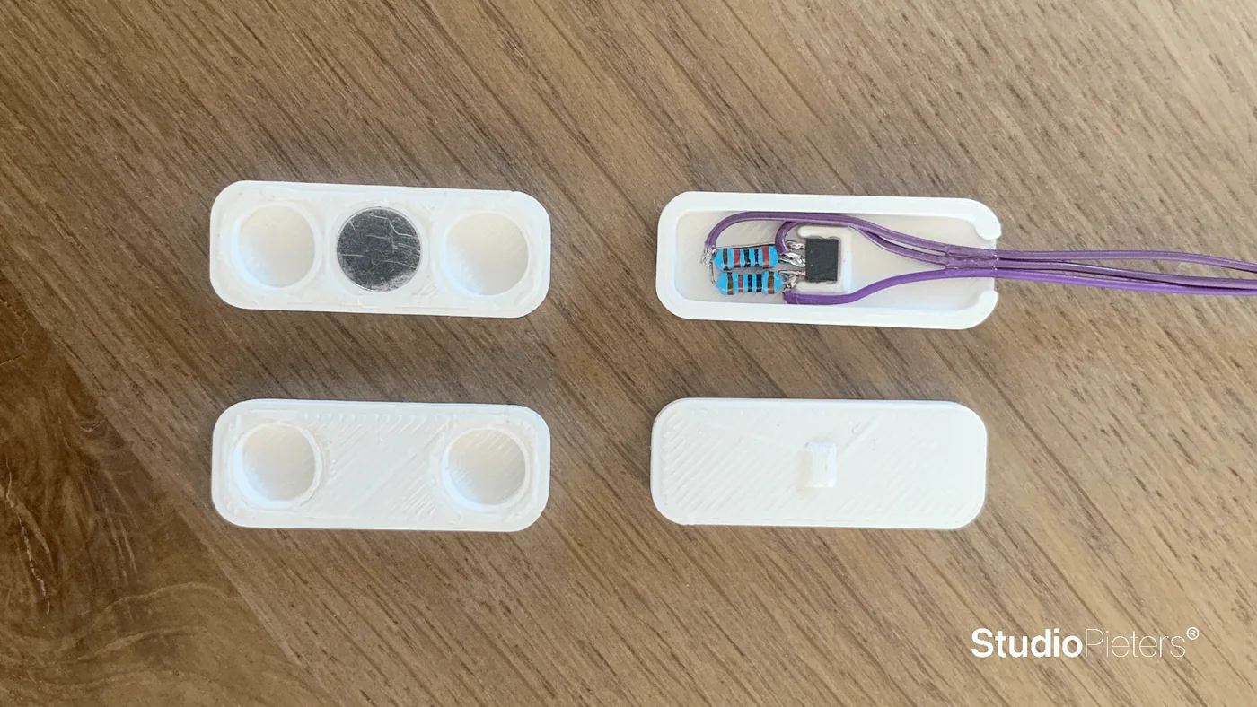The printed test housing parts on a wooden table, one with the sensor and a purple cable fitted