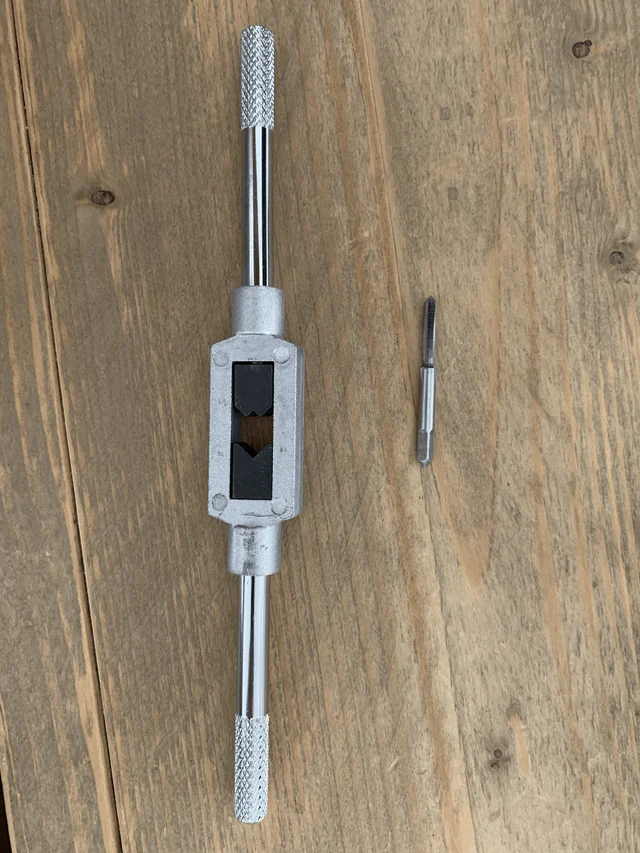A tap wrench and a tap on a wooden table